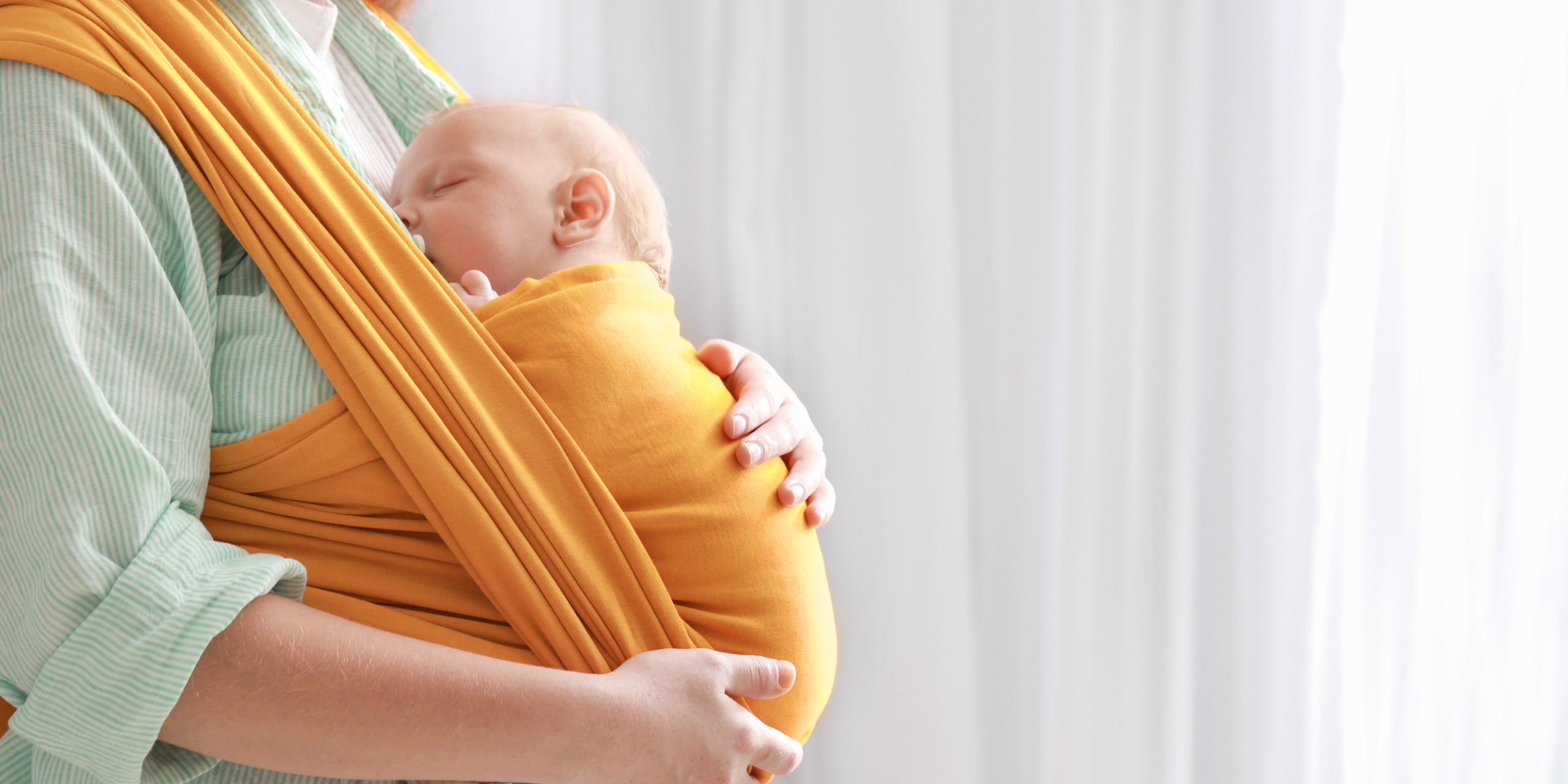 Young mother with little baby in sling at home