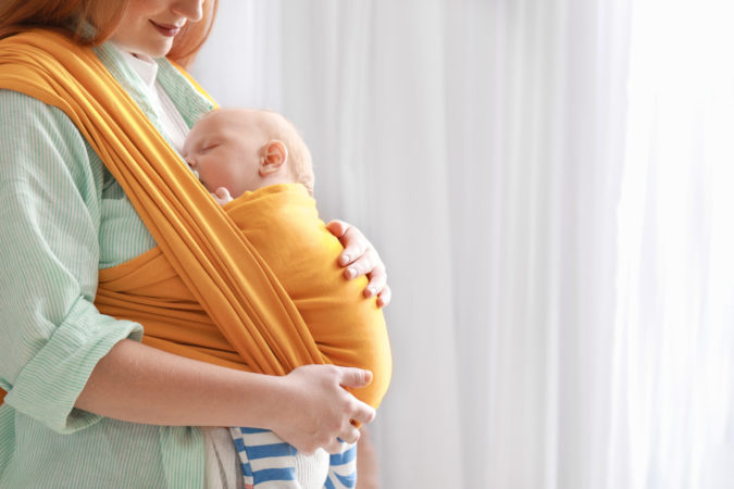 Young mother with little baby in sling at home